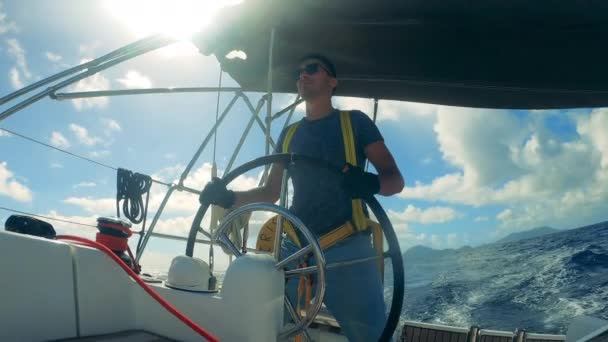 Un hombre con gafas de sol está manejando una rueda de un velero. Océano, velero marítimo controlado por un joven
. - Metraje, vídeo