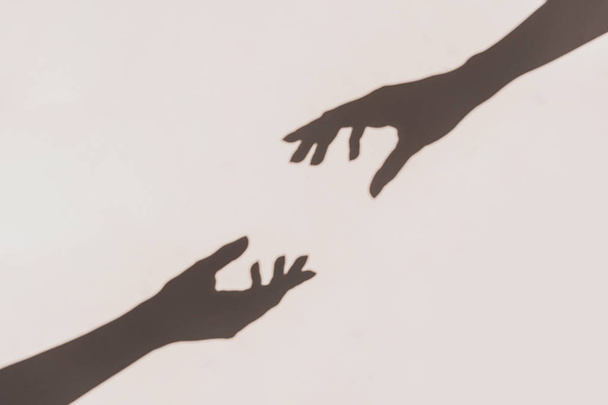 Grey shadows of hands reaching each other on the wall. Abstract blurred effect. - 写真・画像