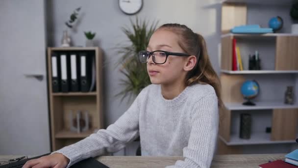 Cute modern focused 15-aged girl in glasses working with computer in her room - Záběry, video