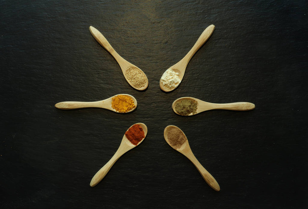 Fotografie von Pulvergewürzen in kleinen Holzlöffeln auf einer Schiefertafel  - Foto, Bild
