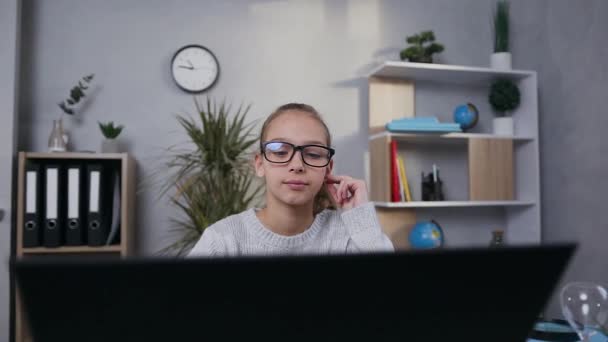 Attractive portrait of serious attantive 15-aged girl in glasses which sitting in front of laptop and searching neccessary information for her hometask - Felvétel, videó