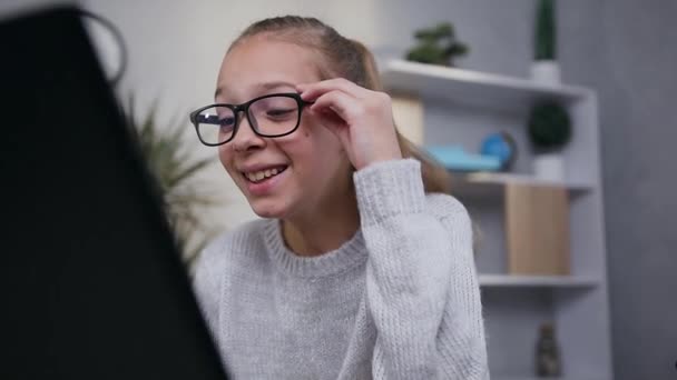Attractive happy smiling teen girl in glasses reading the funny text on laptop screen - Кадры, видео