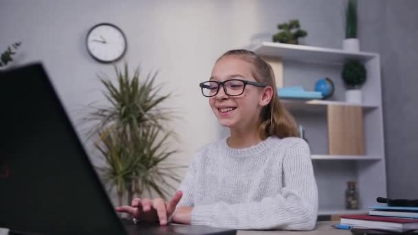 Satisfied cheerful 15-aged girl in gray knitted sweater in eyeglasses smiling from amusing video on screen of computer - Filmati, video