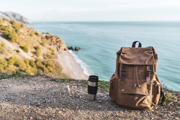 Backpack and coffee thermos with the coast in the background. Concept of exploration and adventures - Fotoğraf, Görsel