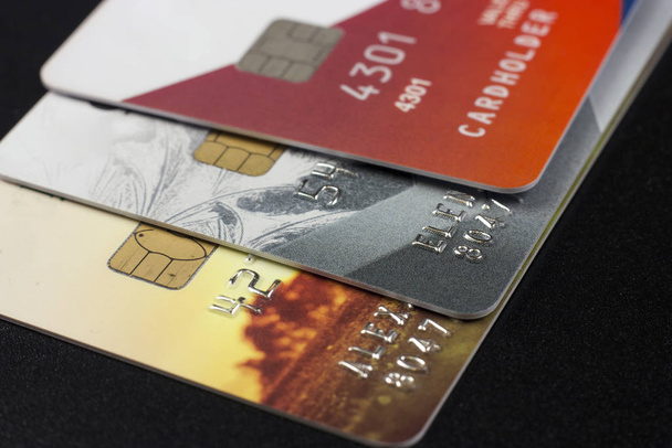 Drie bank creditcards met chips van verschillende kleuren op een zwarte achtergrond - Foto, afbeelding