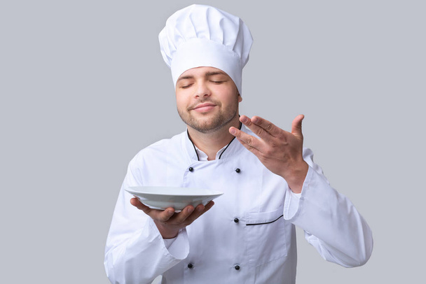 Koch Kerl hält Teller riechende Schüssel posiert über grauen Hintergrund - Foto, Bild