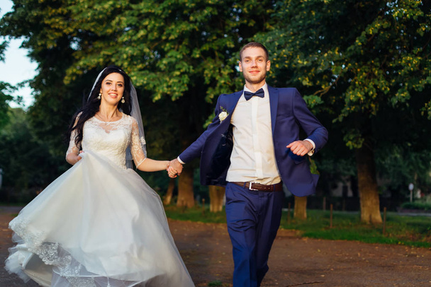 novomanželé se drží za ruce, dívají se do kamery a běží. nevěsta  - Fotografie, Obrázek