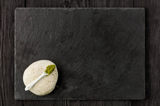 Matcha green tea powder in ceramic spoon on white stone and dark background. - Photo, Image