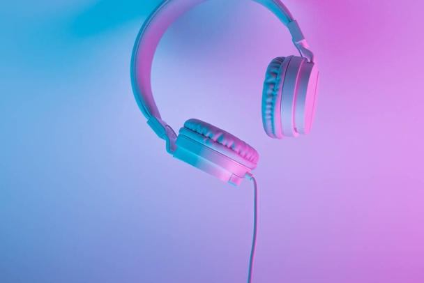 Retro 90s style photo of white stylish wireless headphone in neon lights. Music concept. - Фото, изображение