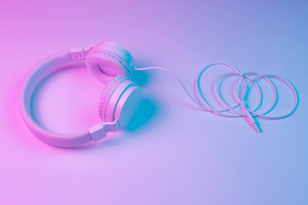 Retro 90s style photo of white stylish wireless headphone in neon lights. Music concept. - Фото, изображение