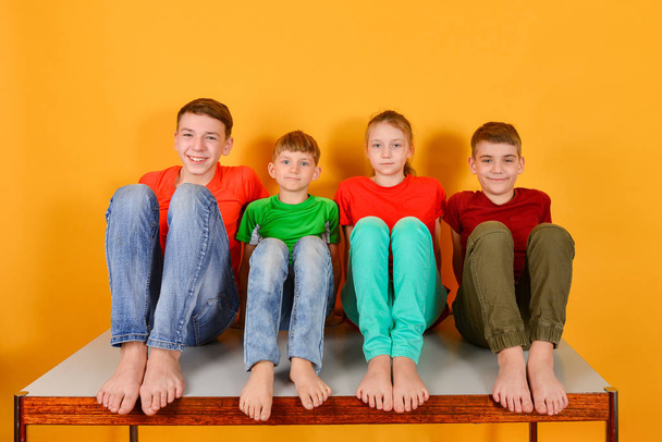 vier Kinder hocken barfuß, ein knallbuntes, saftiges Foto von Teenagern in farbiger Kleidung. - Foto, Bild