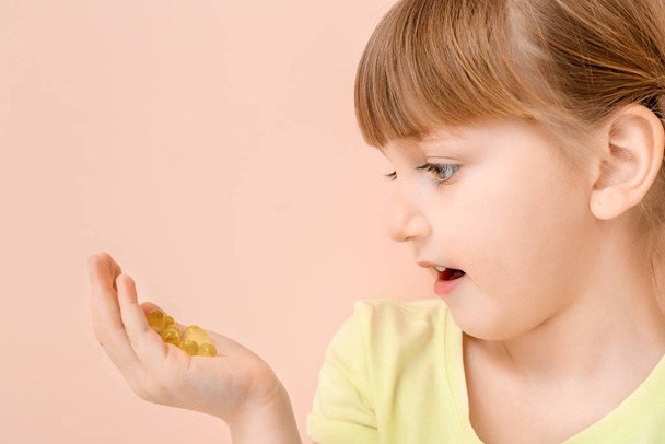 Κοριτσάκι με χάπια ιχθυελαίου στο φόντο χρώμα - Φωτογραφία, εικόνα