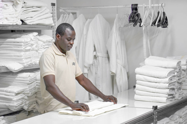 Wäschehotel. älterer afrikanischer Mann legt ein weißes Handtuch aus. - Foto, Bild