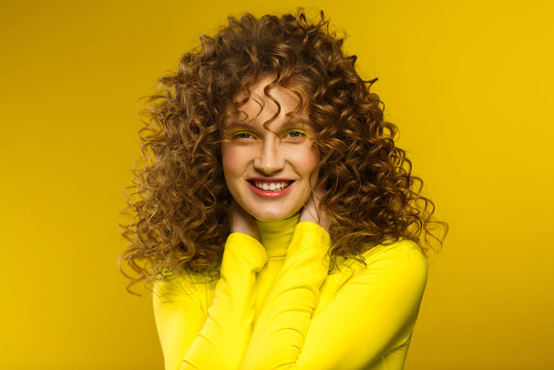 Portrait of young beautiful smiling women with curly hair. Happy girl with wavy hairstyle and bright make up isolated over yellow background. Beauty and hair care concept. Yellow lifestyle. Copy space - Valokuva, kuva
