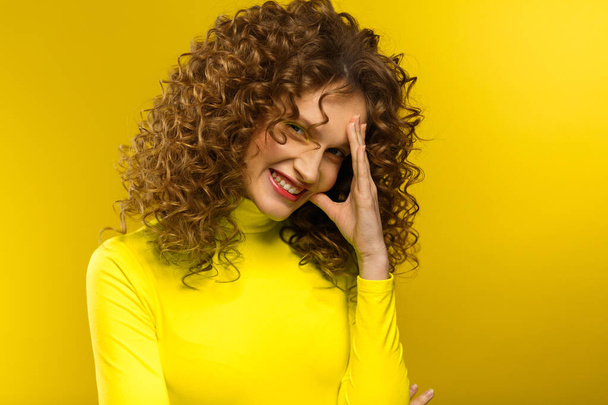Portrait of young beautiful smiling women with curly hair. Happy girl with wavy hairstyle and bright make up isolated over yellow background. Beauty and hair care concept. Yellow lifestyle. Copy space - Photo, image