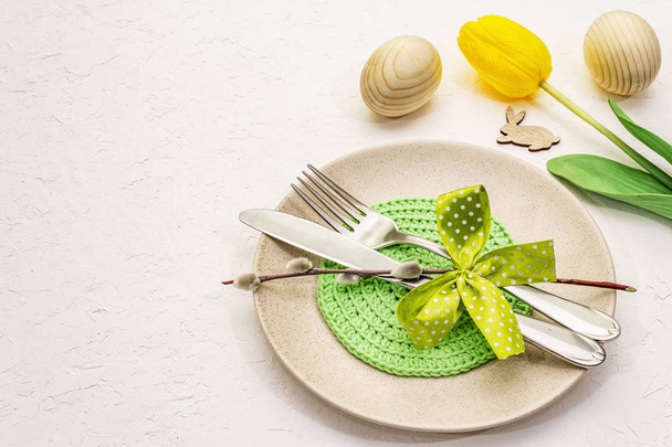Пасхальний стіл на текстурованому білому фоні шпаклівки. Весняний шаблон святкових листівок. Столові прибори, в'язана серветка, яйце, кролик, тюльпан
 - Фото, зображення