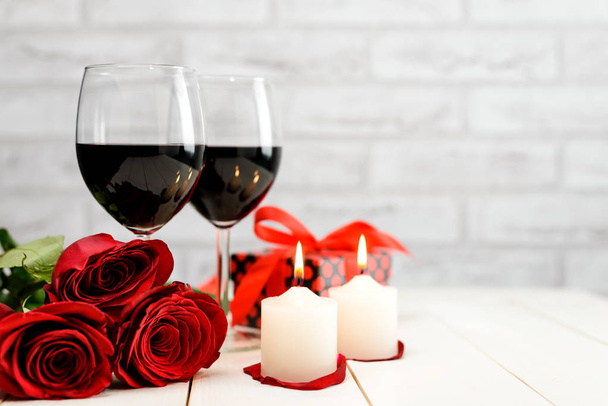 Una copa de vino, rosas, regalos y velas encendidas
 - Foto, imagen