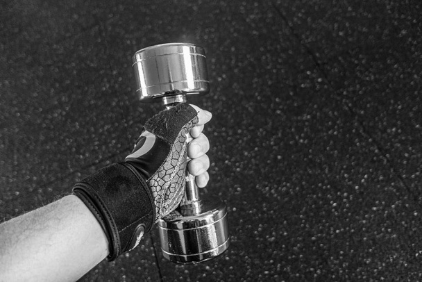 in a gym a hand with a glove is holding a silver dumbbell - Foto, Bild