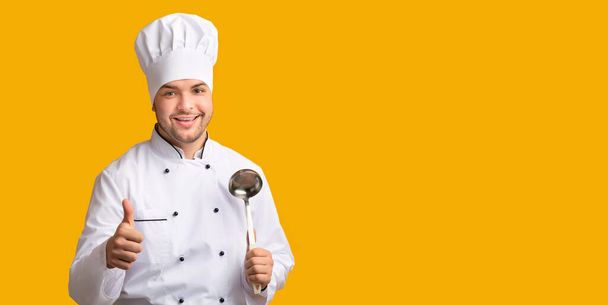 Chef profissional que prende a colher da colher da concha que gere polegares-para cima, fundo amarelo, Panorama
 - Foto, Imagem