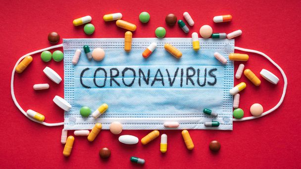 Coronavirus - 2019-ncov, Wuhan virüsü konsepti. Kırmızı arka planda cerrahi maske koruyucu. Coronavirus metninde bir sürü hap var. Çin korona virüsü salgını. - Fotoğraf, Görsel