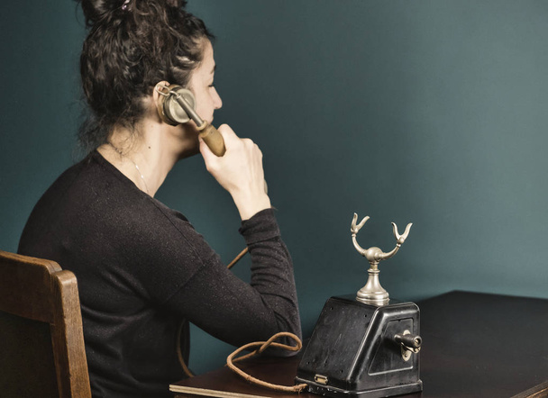 portrait of young Hispanic woman talking on vintage telephone, green wall old brown table - Fotografie, Obrázek