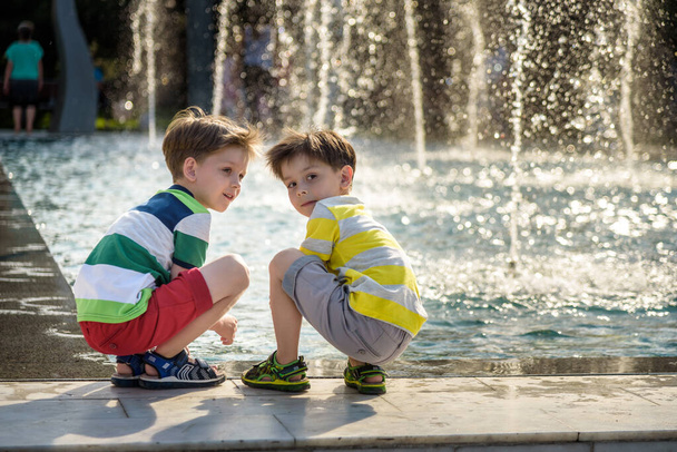 Carino bambino ragazzo e fratelli maggiori, giocando su un getto fontane con spruzzi d'acqua intorno, estate
 - Foto, immagini