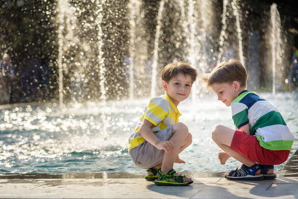 Cute toddler boy and older brothers, playing on a jet fountains with water splashing around, summertime - Photo, Image