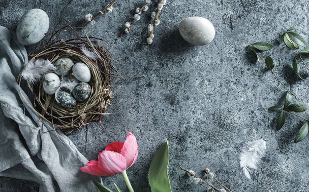 Easter eggs in nest with feathers and red tulips flowers on blue background. Happy Easter holiday, top view, flat lay - Foto, Imagen
