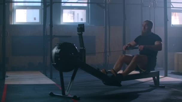 Egy erős, lassított felvételű férfi meghúzza a kötelet egy evezős szimulátorban. Kardio edzés egy embernek egy légköri fitneszteremben. - Felvétel, videó