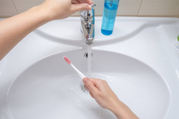 Female hands washing a toothbrush in the bathroom, dental care concept and preparation for teeth cleaning - Photo, image