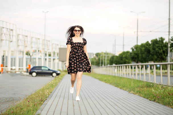 Una mujer sonriente adulta camina por la calle con un vestido elegante. El concepto del estilo de vida, la vida urbana y activa
. - Foto, imagen