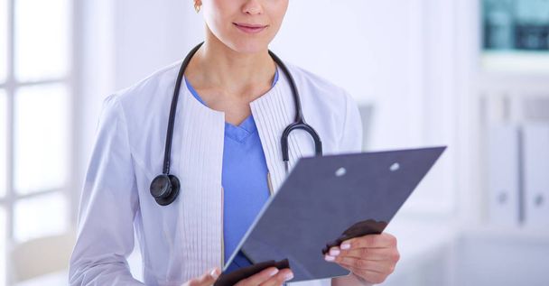 Young smiling female doctor with stethoscope holding a folder at doctors office - Foto, imagen