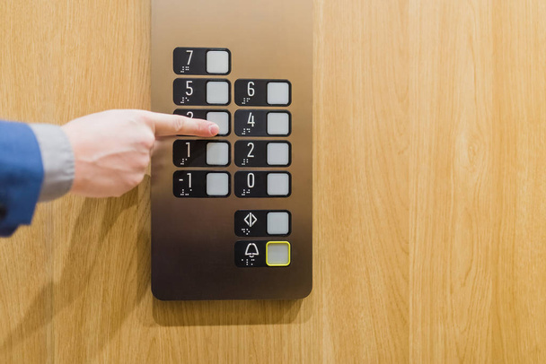 Close up of businessman pressing button in modern wooden and steel elevator. - Foto, Imagen