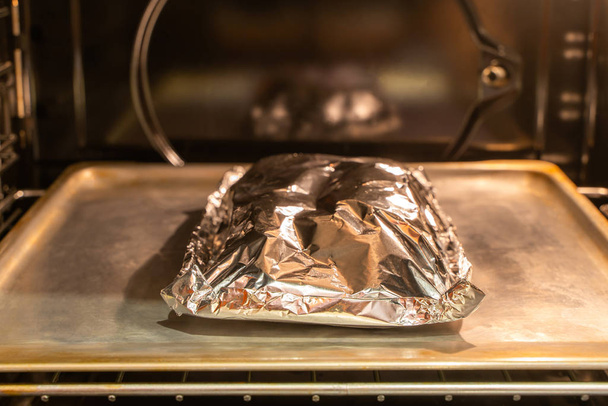 Food covered with foil on the pan inside oven - Valokuva, kuva