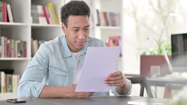 Νεαρός Αφροαμερικανός άνδρας διαβάζει έγγραφα στο γραφείο  - Πλάνα, βίντεο