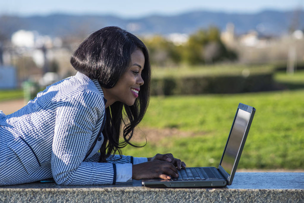 Açık hava parkında dizüstü bilgisayar kullanan Afro-Amerikalı bir kadın. - Fotoğraf, Görsel
