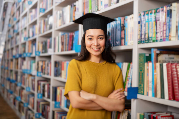 Απόφοιτος κορίτσι μπροστά από μια βιβλιοθήκη. Έννοια της προετοιμασίας και του προσδιορισμού - Φωτογραφία, εικόνα