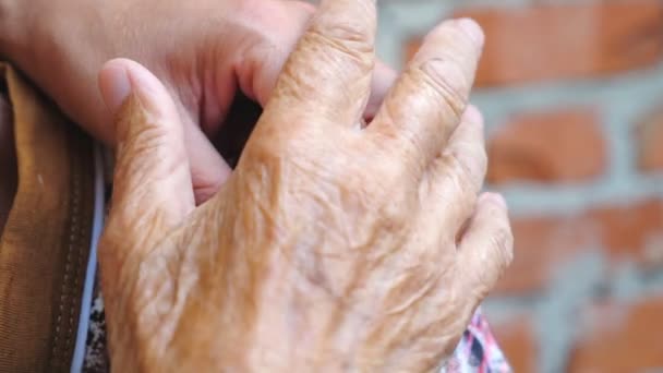 Női ráncos kéz gyengéden simogatja a lánya vállát, törődést vagy szeretetet mutatva. Egy nő, aki támogatja a régi szüleit. Az idős anya vigasztaló karja. Meleg családi kapcsolatok - Felvétel, videó