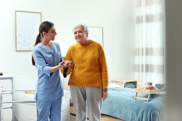 Care worker helping elderly woman to walk in geriatric hospice - Zdjęcie, obraz