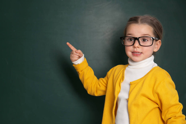 Cute little child wearing glasses near chalkboard. First time at - Foto, Imagen