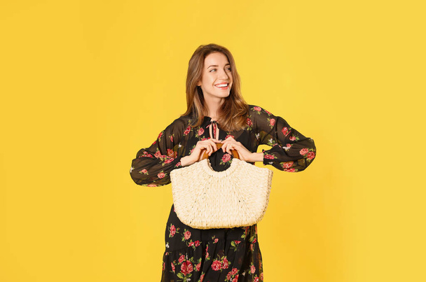 Young woman wearing floral print dress with straw bag on yellow  - Foto, imagen