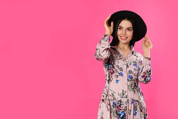 Young woman wearing floral print dress and stylish hat on pink b - Foto, imagen