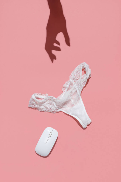 The concept of an erotic chat worker. White lace panties, wireless mouse and female hand shadow on a pink background - Foto, Imagem