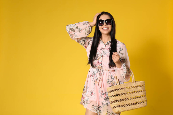Young woman wearing floral print dress with straw bag on yellow  - Foto, Bild