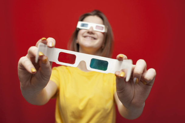 funny girl in 3D glasses on a red background gives glasses, offers to watch a movie - 写真・画像