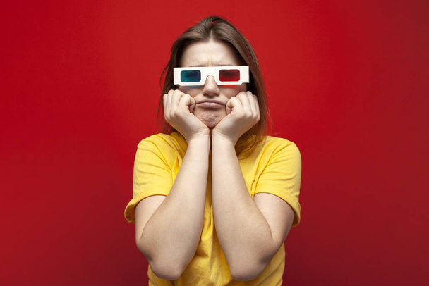 sad young girl watching a bad, boring movie in 3d glasses and with popcorn on a red background - Photo, Image