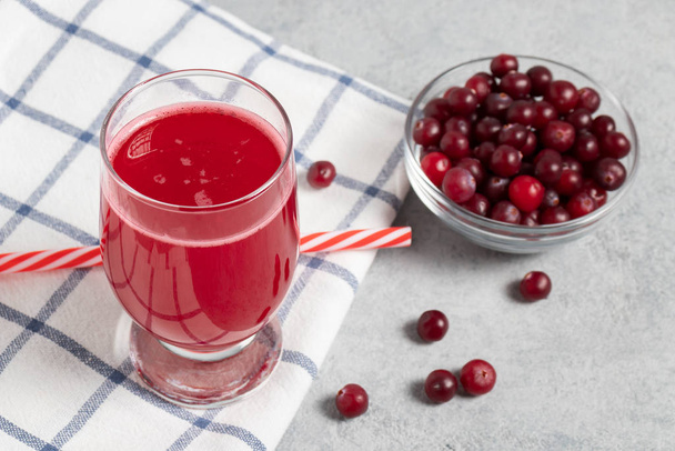 One glasses with homemade freshly cranberry juice and a bowl of cranberries on a gray concrete table - Zdjęcie, obraz