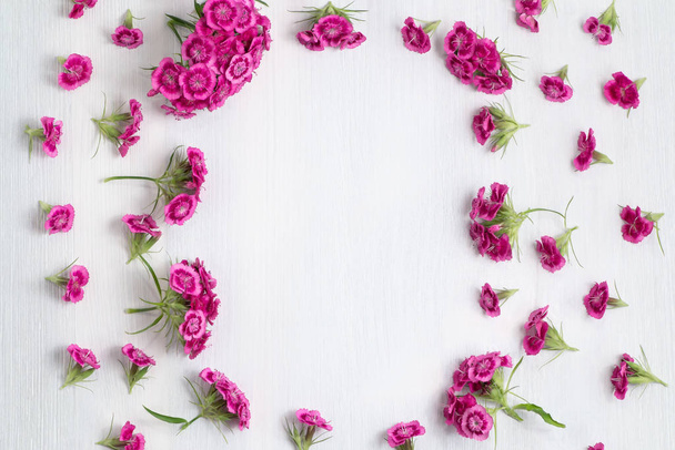 Floral arrangement with copy space. Template for greeting card or design. Frame of pink carnations on a white wooden background - Fotografie, Obrázek