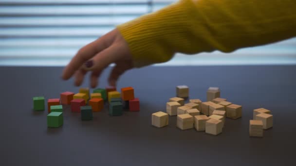 Young female hand with a red manicure in sweater mixing coloured wooden blocks with uncoloured and puting green block on top of others. Closeup video where girl playing with the wooden blocks. - Imágenes, Vídeo