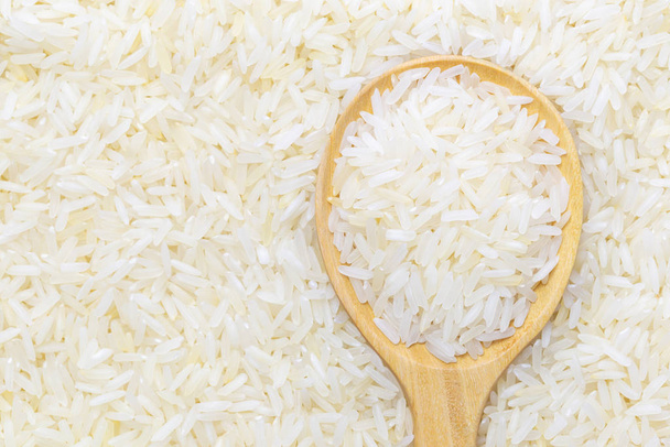 Thai jasmine rice in wooden spoon over rice background. - Photo, Image